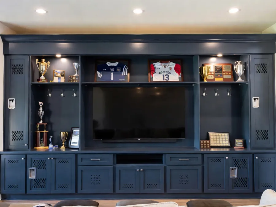 Navy built-in trophy and jersey display wall with locker doors around a TV, by Desert Forge Cabinets